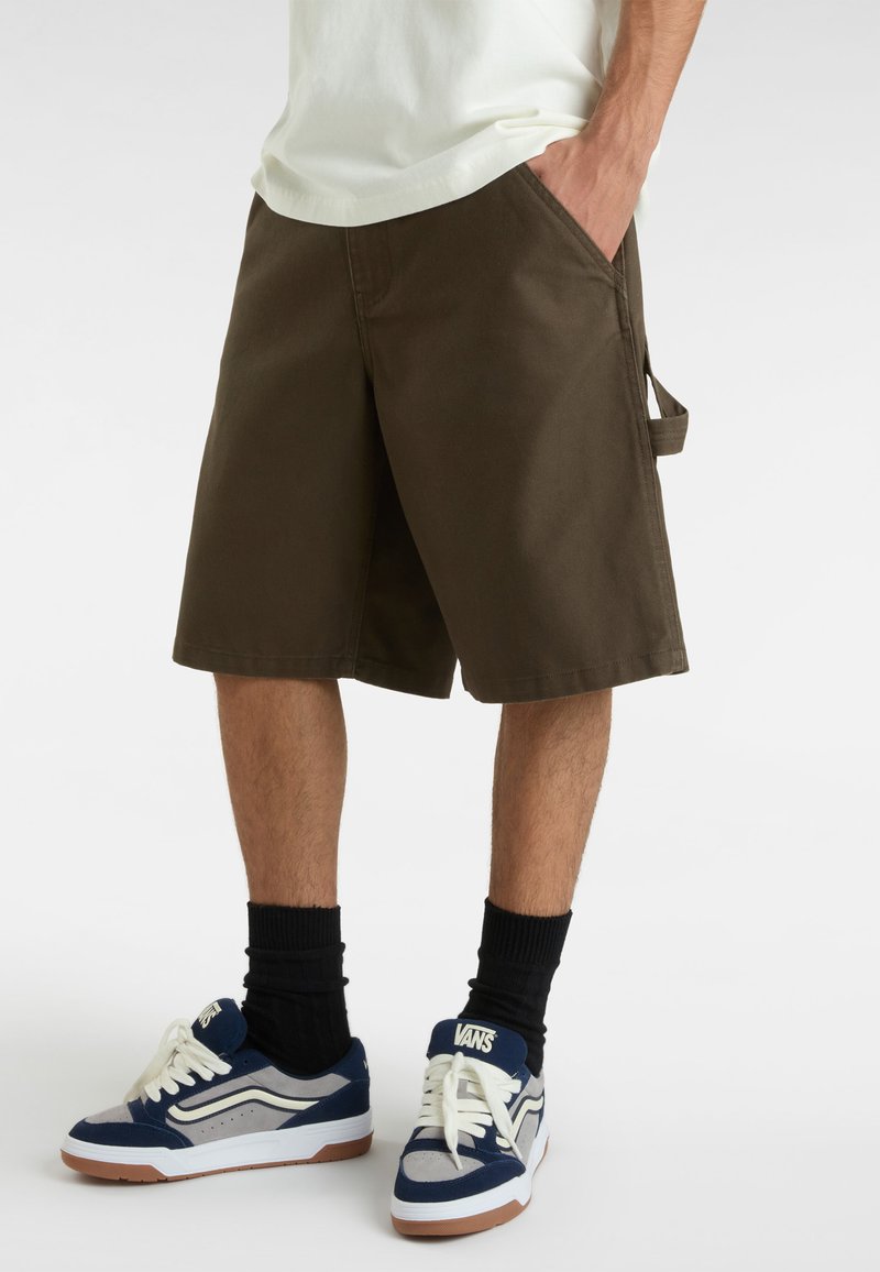 Braune Baumwollshorts mit zwei seitlichen Taschen, seitlicher Riemendetail, getragen mit Vans Sneakers in Marineblau, Grau und Weiß.