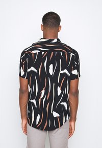Korte mouwen shirt met een zwarte basis en abstracte, meerkleurige penseelstreekpatronen in wit, beige en roest. Standaardkraag en afgeronde zoom.