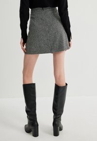 Minifalda de tweed gris con cintura ajustada, combinada con altas botas de cuero negras. La tela tiene un acabado texturizado y un patrón sutil.
