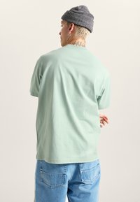 Mintgrøn bomulds T-shirt med en afslappet pasform, korte ærmer og rund halsudskæring, båret med lyseblå denim jeans.