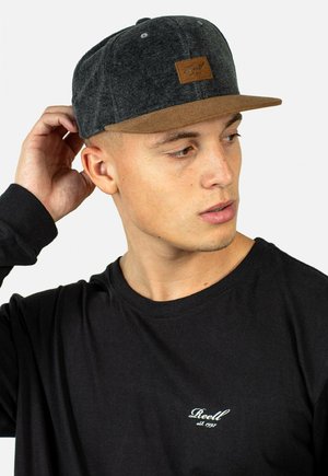 Schwarze Snapback-Basecap mit einem grauen Filzkorpus und einem beigen Wildleder-Schirm. Verfügt über ein kleines braunes Lederetikett auf der Vorderseite. Getragen mit einem schwarzen Langarmshirt.