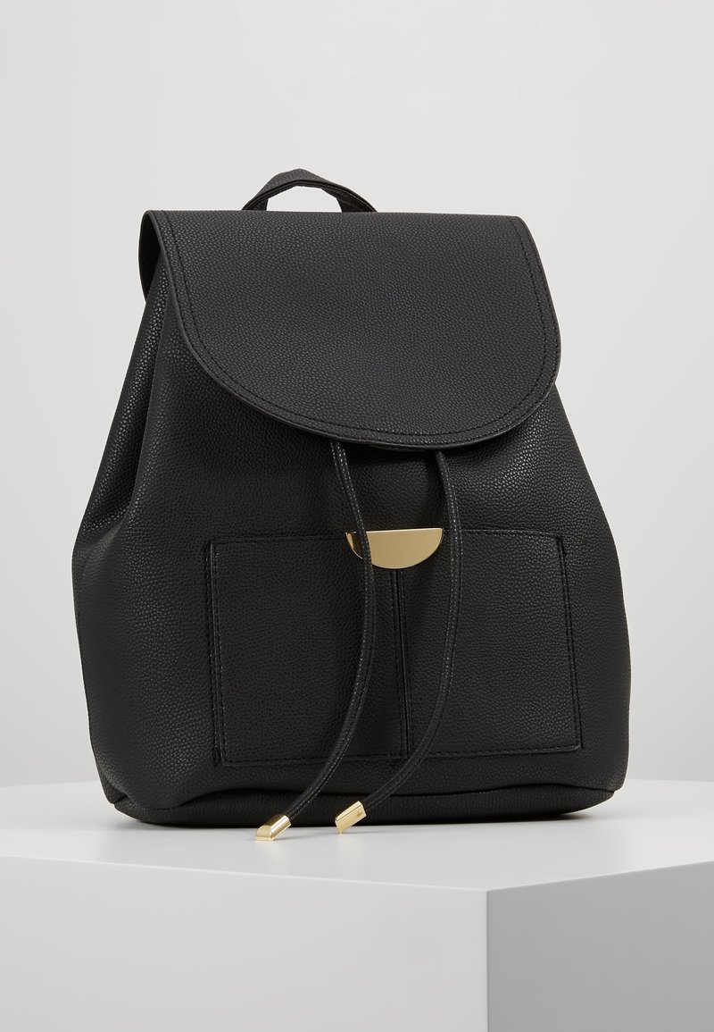 Sac à dos en cuir texturé noir avec poche avant, fermeture par rabat, cordons réglables avec embouts en métal doré et poignée de transport supérieure.