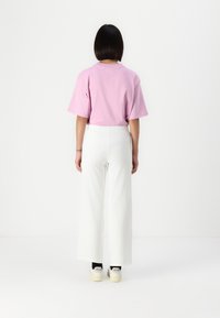 Pink cotton t-shirt, oversized fit, paired with white wide-leg pants. Sneakers with black accents and "VEJA" branding visible.