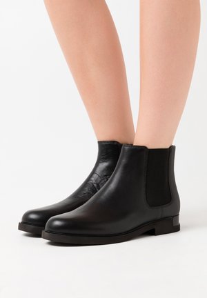 Bottines en cuir noir avec une finition lisse, des panneaux latéraux élastiques et des semelles en caoutchouc plates. Design minimaliste avec un bout rond.