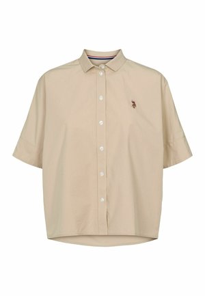 Béžová košeľa s krátkym rukávom a golierom na gombíky, s malým vyšívaným logom na ľavej strane hrude a hladkou textúrou látky.