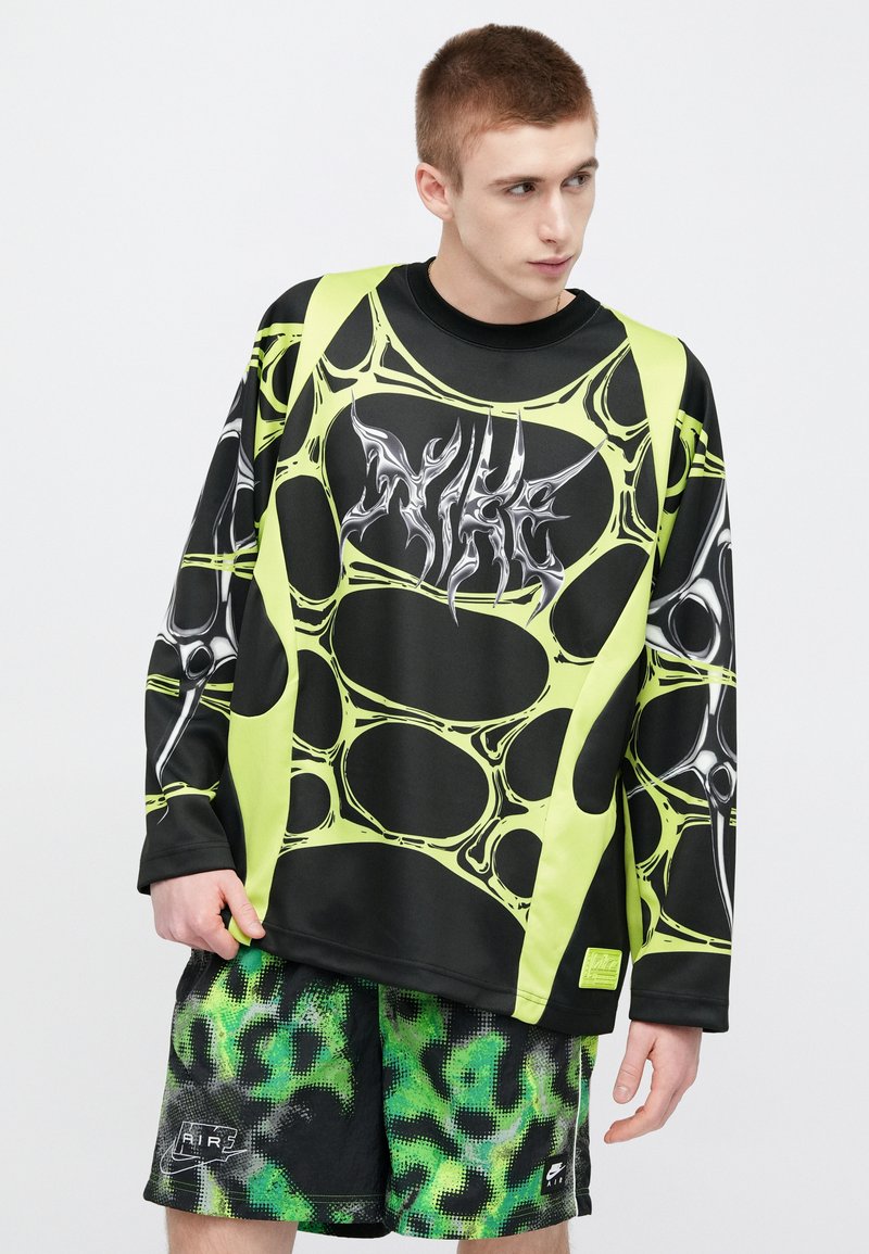 Black and neon green long-sleeve shirt with abstract bubble pattern and silver graphic. Paired with black and green patterned shorts.