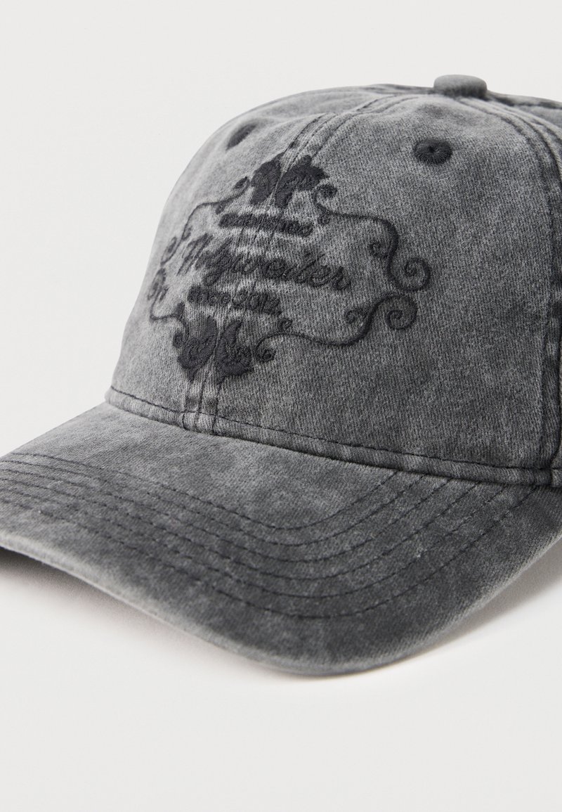 Grijze honkbalpet met gebogen klep, zwart geborduurd sierlijk ontwerp en deels leesbare cursieve tekst op het voorpaneel.