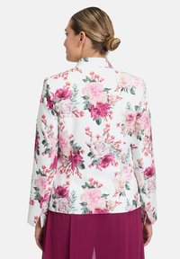 Kwiatowa marynarka w białym kolorze z intensywnymi różowymi i różowymi wzorami, dopasowany kształt i długie rękawy. Posiada klapowy kołnierz i gładką teksturę.