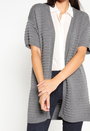Cardigan grigio lavorato a maglia con maniche corte, texture a coste e design aperto. Abbinato a una camicia bianca con colletto e pantaloni scuri.