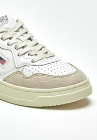 Sneaker in pelle bianca con dettagli in suede beige, punta traforata e suola in gomma color crema. Presenta cuciture decorative e lacci.