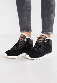 Svarta och grå quiltade högskor med vita sulor, ullfoder och mönstrade skosnören, bärs med mörkgrå uppvikta jeans.