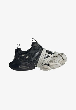Sneaker bicolore nero e bianco con suola spessa, caratterizzata da lacci bianchi avvolti in modo lasco intorno al mesopiede e all’area delle dita.