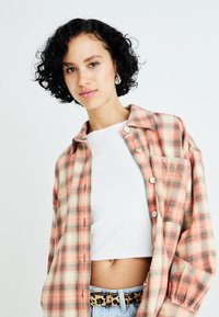 Rutete skjorte i fersken, creme og grønne farver, lavet af blødt stof. Bæres over en hvid cropped top og har en brystlomme.
