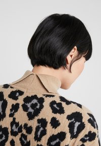 Suéter beige con un estampado de leopardo negro y gris, que cuenta con un cuello acanalado y mangas cortas texturizadas.