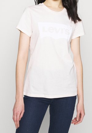 Jasnoróżowa bawełniana koszulka z białym logo Levi's na przodzie, okrągły dekolt i krótkie rękawy, w zestawie z ciemnymi dżinsami.