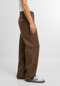 Braune, weit geschnittene Hosen aus strapazierfähigem Baumwollstoff. Verfügt über Seitentaschen und ein besticktes Logo-Detail über der Gesäßtasche.