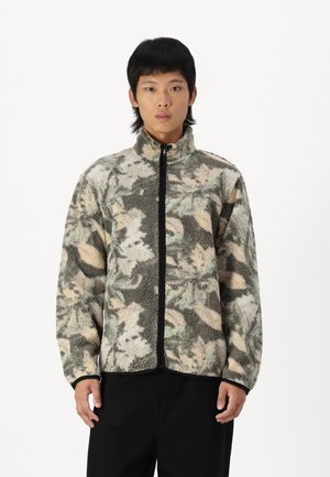 Fleecejack met een hoge kraag, voorzien van een bloemen camouflagedessin in groen, bruin en beige; zwarte ritssluiting en mouwen.