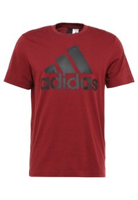 Punainen puuvillapaita, jossa on pyöreä pääntie ja musta Adidas-logo sekä kolme mustaa raitaa edessä, lyhyet hihat.