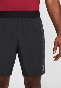 Calções atléticos pretos com textura suave, cós elástico, bolso lateral e um pequeno logótipo branco na parte inferior lateral.