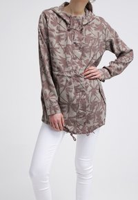 Lätt huvad jacka i dämpad beige med ett brunt palmbladsmönster, med cinchad midja och framknäppning. Matchad med vita byxor.