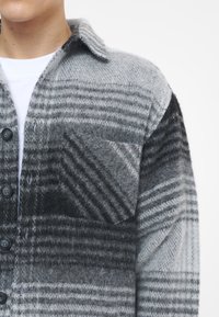 Camicia a bottoni in misto lana grigia e nera, con motivo a quadri, colletto a punta, taschino singolo e tessuto testurizzato.