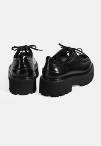 Zwarte leren platform schoenen met ronde neuzen, gestructureerd oppervlak, chunky zool en vetersluiting. De achterzijde benadrukt het verhoogde ontwerp.