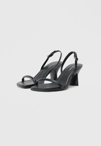 Black slingback heeled sandals feature thin straps and a square toe. The heels have a block design with a smooth leather finish.