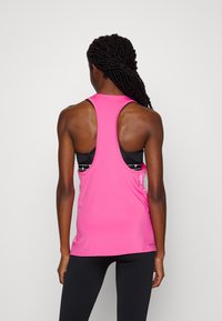 Hihaton urheilumaila kirkkaan vaaleanpunaisesta kankaasta, jossa on racerback-muotoilu; alla näkyy musta urheilBra.