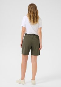 Shorts vert kaki avec une taille élastique, arrivant au milieu de la cuisse, associés à un t-shirt blanc uni. Tissu doux, design décontracté.