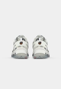 Sandalias deportivas blancas y grises con múltiples correas, suela texturizada y detalle de logo prominente en el talón. Material de goma, diseño abierto.