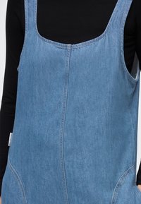 Denimkjole med firkantet utringning og brede stropper, med et lyst blått stoff med glatt tekstur og subtile søm detaljer.