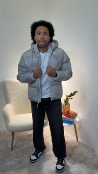 Veste matelassée grise à finition texturée, dotée d'une capuche, de deux poches avant, portée avec un T-shirt blanc. Jean noir et baskets.