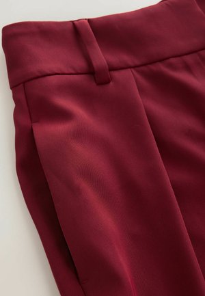 Burgundské kalhoty s hladkým texture, polově zúžený střih a přední záhyby. Mají široký pas a boční kapsy.