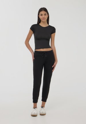 Top aderente nero a maniche corte abbinato a jogger neri con vita regolabile, polsini e scarpe da ginnastica bianche. Tessuto liscio.