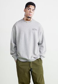 Gray sweatshirt with a crew neck, ribbed cuffs, and a mountain logo on the chest, paired with olive green pants. Soft fabric texture.