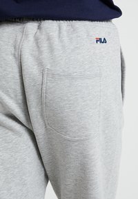 Grå sweatpants med en enda bakficka och en FILA-logotyp i röd och blå. Tillverkade av mjukt, texturerat material med resårmidja.