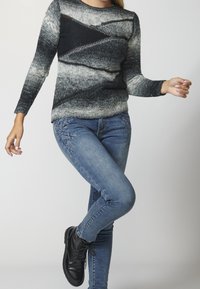 Neulottu villapaita, jossa on harmaa-musta liukuvärjäys ja kuvioitu rakenne, yhdistetty sinisiin farkkuihin, joissa on kukka-aiheista kirjailua, sekä mustiin saappaisiin.