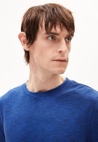 Blauwe, gestructureerde t-shirt met een ronde hals en korte mouwen. De stof heeft een subtiel gestreept patroon. Model heeft kort haar.