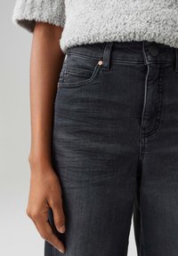 Jeans in denim nero con taglio dritto, dotati di un design a cinque tasche e accenti in hardware rame. Il tessuto ha una texture liscia e usurata.