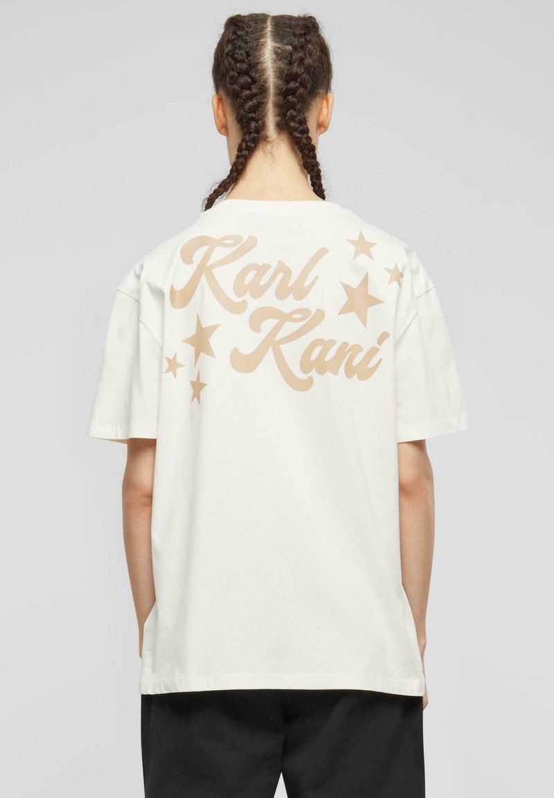 Cremefarvet bomulds T-shirt med stor tan tekst, der læser "Karl Kani" med stjernedetaljer på ryggen. Løs pasform, korte ærmer og enkelt design.
