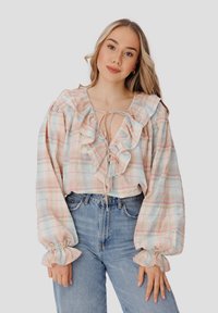 Blusa de cuadros ligera en colores pastel, con un cuello y mangas con volantes, cierre con lazo y mangas globo voluminosas.