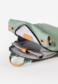Groene roll-top rugzak gemaakt van waterdicht materiaal met beige leren accenten, met een ruime grijs geruite interieur en organisatorische zakken.
