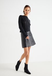 Top negro texturizado de manga larga combinado con una falda corta de cuero negra en línea A y botas negras de tobillo con punta afilada y tacón cuadrado.