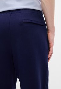 Sötétkék pamut nadrág, hátul egy diszkrét varrással ellátott zsebbel. Az anyag simának és könnyűnek tűnik, rugalmas derékpánttal.