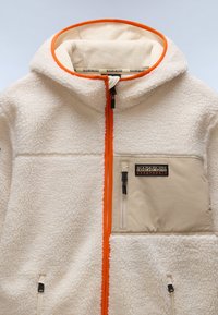Krämsfärgad fleecejacka med orange dragkedjedetalj, beige bröstficka med dragkedja och "Napapijri Geographic" logotyp.