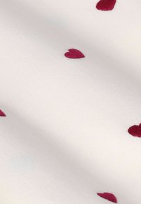 Tissu blanc avec de petits cœurs rouges brodés éparpillés, créant un motif simple et délicat sur une surface lisse.