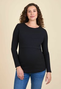 Top lung cu maneci lungi, negru, cu decolteu rotund și corp ajustat, asortat cu blugi din denim albastru. Textură netedă și design simplu.