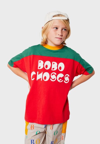 Červené a zelené tričko s krátkym rukávom, na ktorom je v bielej farbe vytlačený nápis "BOBO CHOSES". Okrúhly výstrih, bavlnený materiál, voľný strih a výrazné farebné blokovanie.