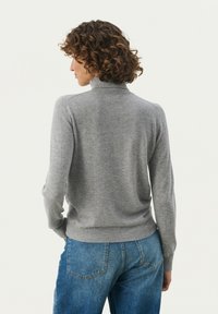 Grå uldblandings sweater med høj hals, tætsiddende lange ærmer og ribkant. Aftalt med blå denim jeans. Teksturen virker blød.