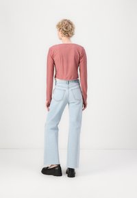 Top cu maneci lungi, în carouri roșii și albe, design scurt, asortat cu blugi largi de un albastru deschis și pantofi cu talpă groasă de culoare neagră.
